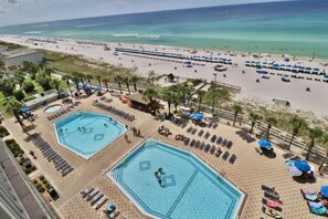 A resort with two large swimming pools, a beach area, and a view of the ocean.