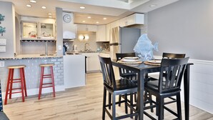 A modern kitchen with a central island, wooden stools, and a dining table with chairs.