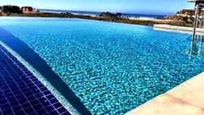 A clear blue infinity pool with a view of the ocean and beach in the background.