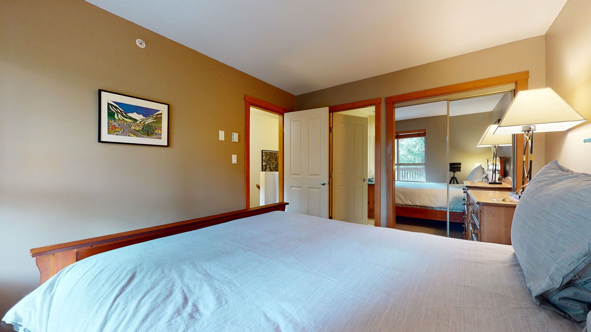 Habitación de hotel con una cama grande, un escritorio con lámpara, una silla, una mesita y un cuadro en la pared.