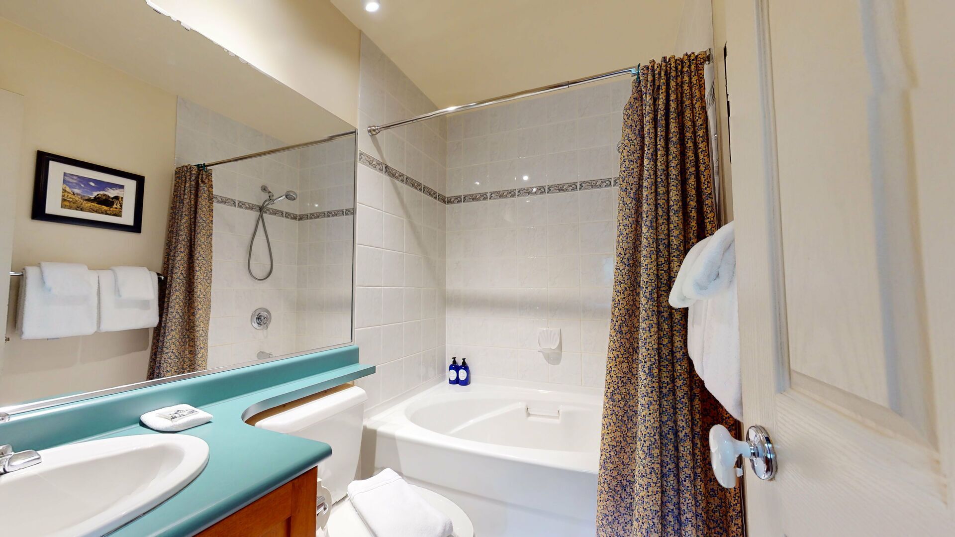 Un baño con dos lavamanos, una bañera, una ducha e inodoro. Hay un perchero con toallas, un cuadro en la pared y un espejo.