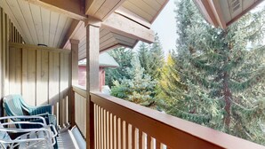 Un balcon en bois offrant une vue sur de grands arbres à feuilles persistantes.