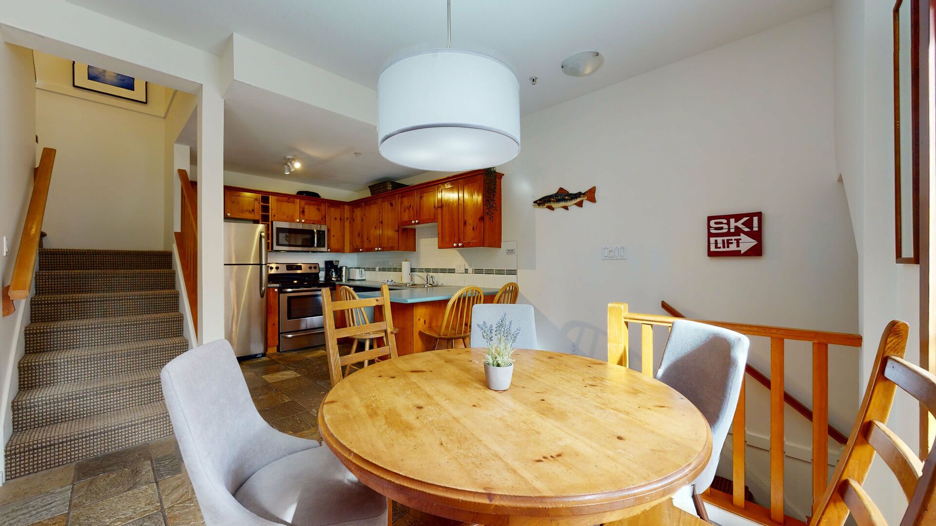 Un coin repas comprenant une table ronde en bois, quatre chaises et un luminaire suspendu.