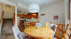 Un comedor con una mesa redonda de madera, cuatro sillas y una lámpara colgante.