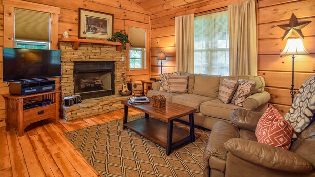 A cozy cabin interior with a stone fireplace, a television, a sofa, and a star-shaped wall decoration. - Smoky Mountain Top Cabin, New Hot Tub, 10 mins to Gatlinburg or Pigeon Forge (Sevierville)