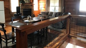 A cozy cabin interior with a wooden dining area, a fireplace, a sofa, and a balcony with a railing. - Smoky Mountain Top Cabin, New Hot Tub, 10 mins to Gatlinburg or Pigeon Forge (Sevierville)