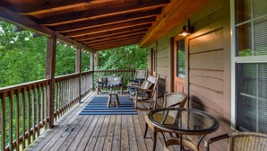 A wooden deck with a covered porch, furnished with a sofa, chairs, and a glass table. - Smoky Mountain Top Cabin, New Hot Tub, 10 mins to Gatlinburg or Pigeon Forge (Sevierville)