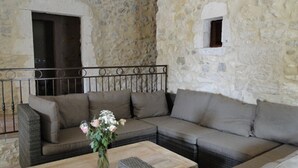 Ein Zimmer mit Steinwänden, einem Ecksofa und einem kleinen Tisch mit Blumen in einer Vase.