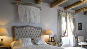 Ein Schlafzimmer mit einem großen Bett, zwei Nachttischen mit Lampen, einem Sessel und einem Fenster mit Vorhängen.