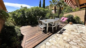 Eine Terrasse mit Holzdeck und Steinböden, umgeben von üppiger Vegetation und Palmen.