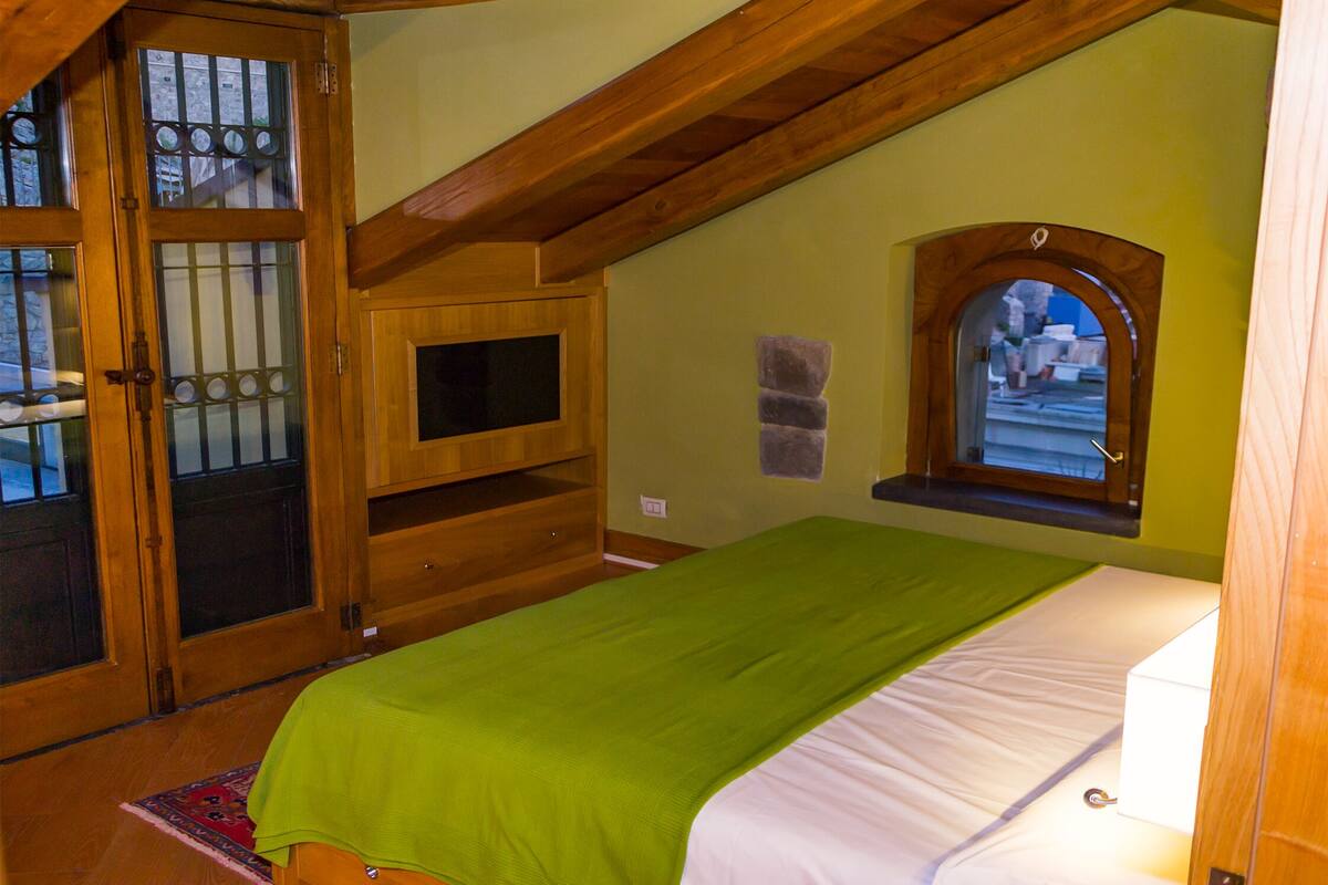 Un dormitorio con cama, puerta de madera con paneles de vidrio, una ventana pequeña y un estante de madera.