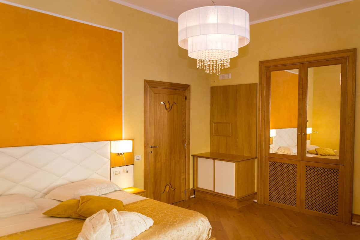 Una habitación de hotel con cama, lámparas de noche, armario y espejo.