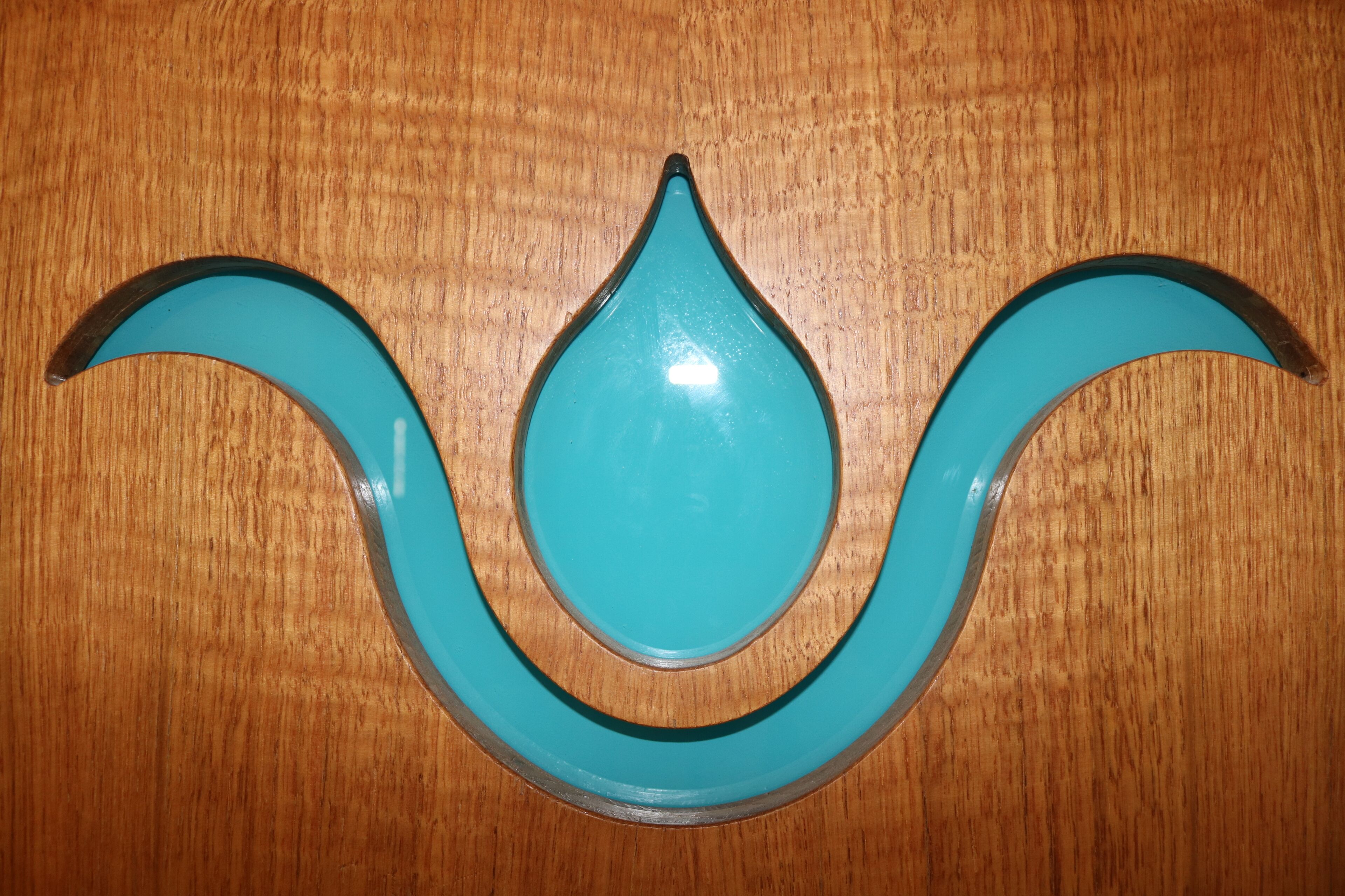 A teal-colored, teardrop-shaped object with a black outline on a wooden surface.