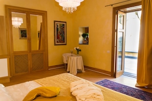 A hotel room with a bed, a small table with a vase and flowers, a painting on the wall, and a door leading to a balcony. - Villa Di Natale (Pagani)