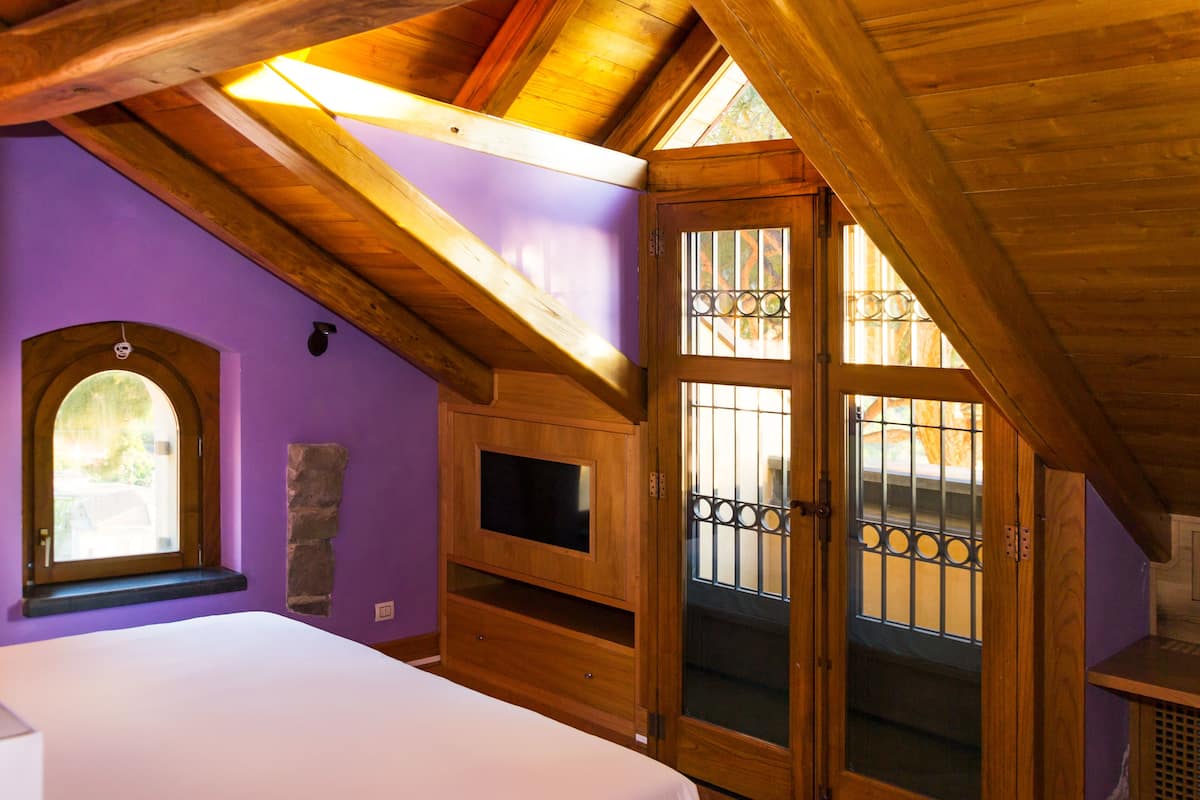 Un dormitorio con techo de madera, televisor empotrado, ventana y puerta con vidrio de seguridad.