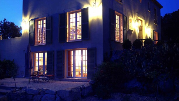 Una casa de dos pisos con muchas ventanas y un patio con mobiliario exterior.