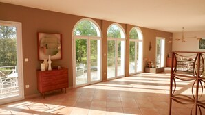 Una habitación amplia con ventanas arqueadas grandes, un armario de madera y una zona de comedor con sillas y una mesa.