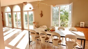 Un comedor con una mesa grande, sillas blancas y un frutero.