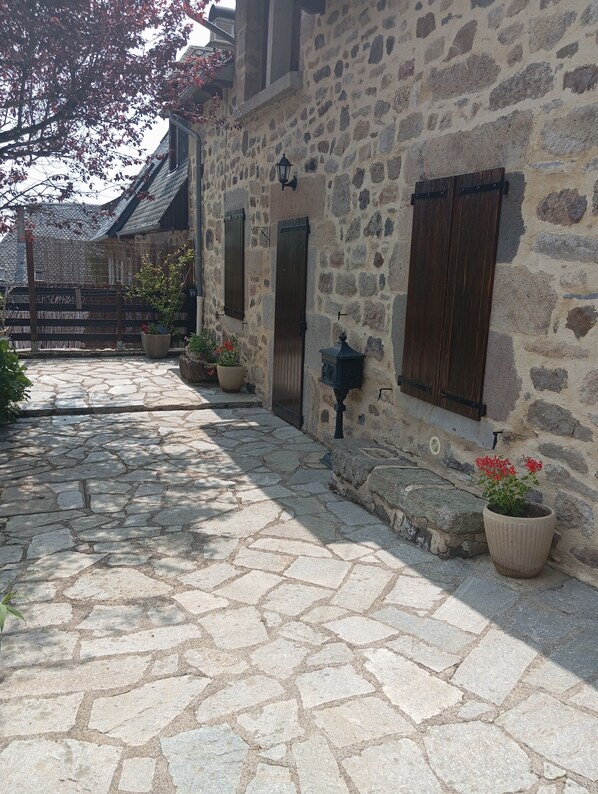 A stone building with a courtyard, potted plants, and a wooden gate.