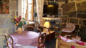 Ein gemütliches Zimmer mit Steinsandsteinwand, einem an der Wand über einem Kamin befestigten Fernseher, einem Esstisch mit Stühlen und einer Holzdressoir.
