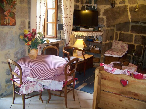 A cozy room with a stone wall, a television mounted above a fireplace, a dining table with chairs, and a wooden dresser. - giteduplombducantal to the guards in Saint-Jacques-Des-Blats (Saint-Jacques-des-Blats)