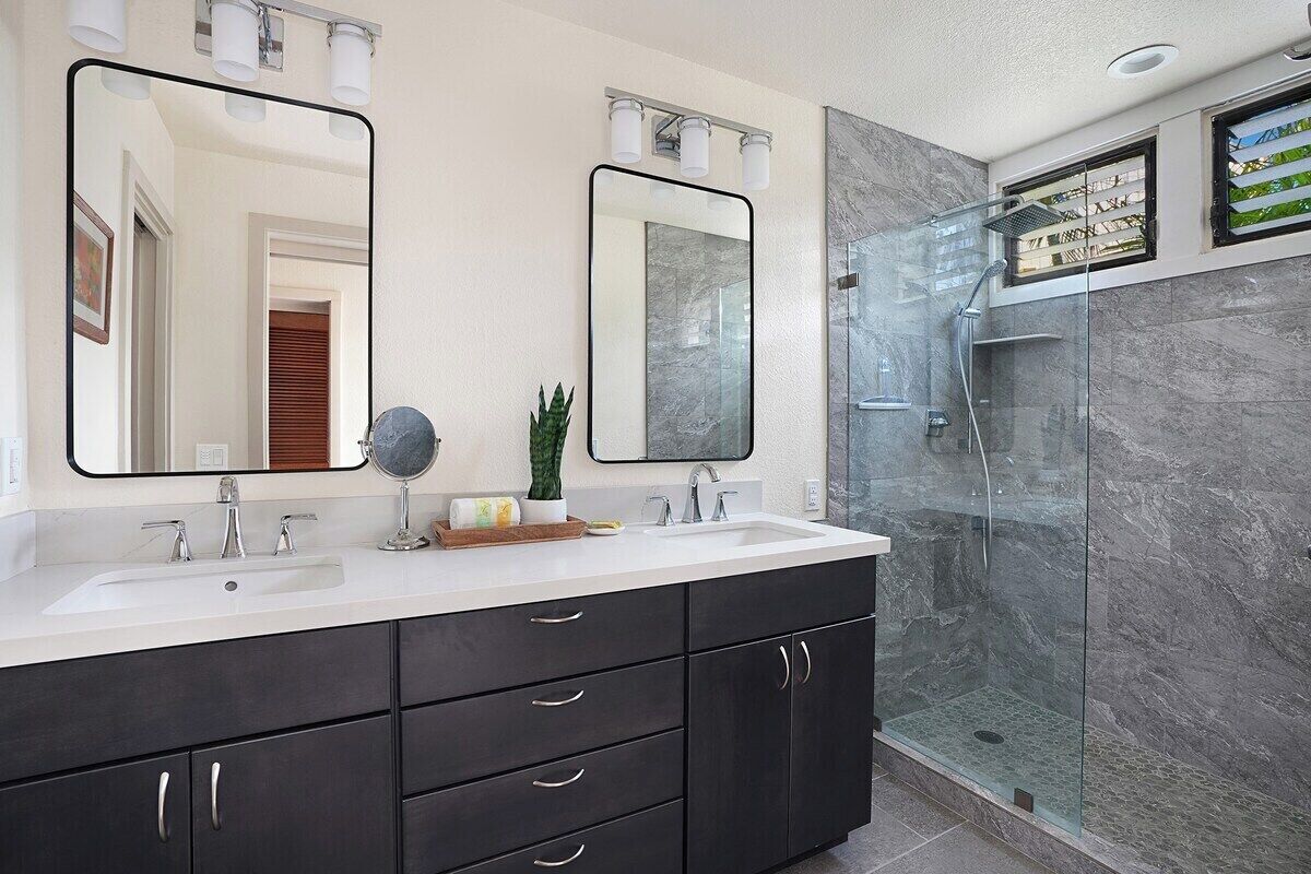 A modern bathroom with a double sink vanity, two large mirrors, a glass shower enclosure, and a marble backsplash.