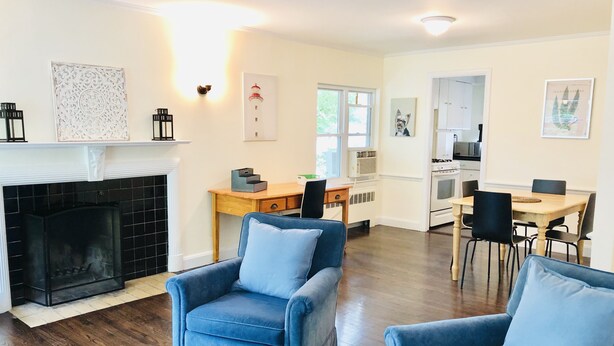 A living room with a fireplace, two blue armchairs, a wooden coffee table, and a dining area with a table and chairs. - Unit2 GR8 LOCATION mins to Longwood Medical Area, BC, BU, HarvMedSchool SPACIOUS (Brookline)