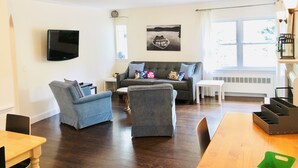 A living room with a grey sofa, two armchairs, a small table, and a TV mounted on the wall. - Unit2 GR8 LOCATION mins to Longwood Medical Area, BC, BU, HarvMedSchool SPACIOUS (Brookline)
