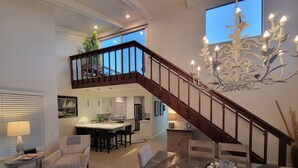 A spacious living area with a dining table, chairs, a chandelier, and a staircase leading to an upper level. - Luv Oceanside-1 House to Beach (San Diego)