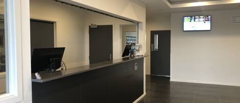 A reception area with a black counter, a television mounted on the wall, and a sign indicating amenities like toilets, gym, cafe, and elevator.