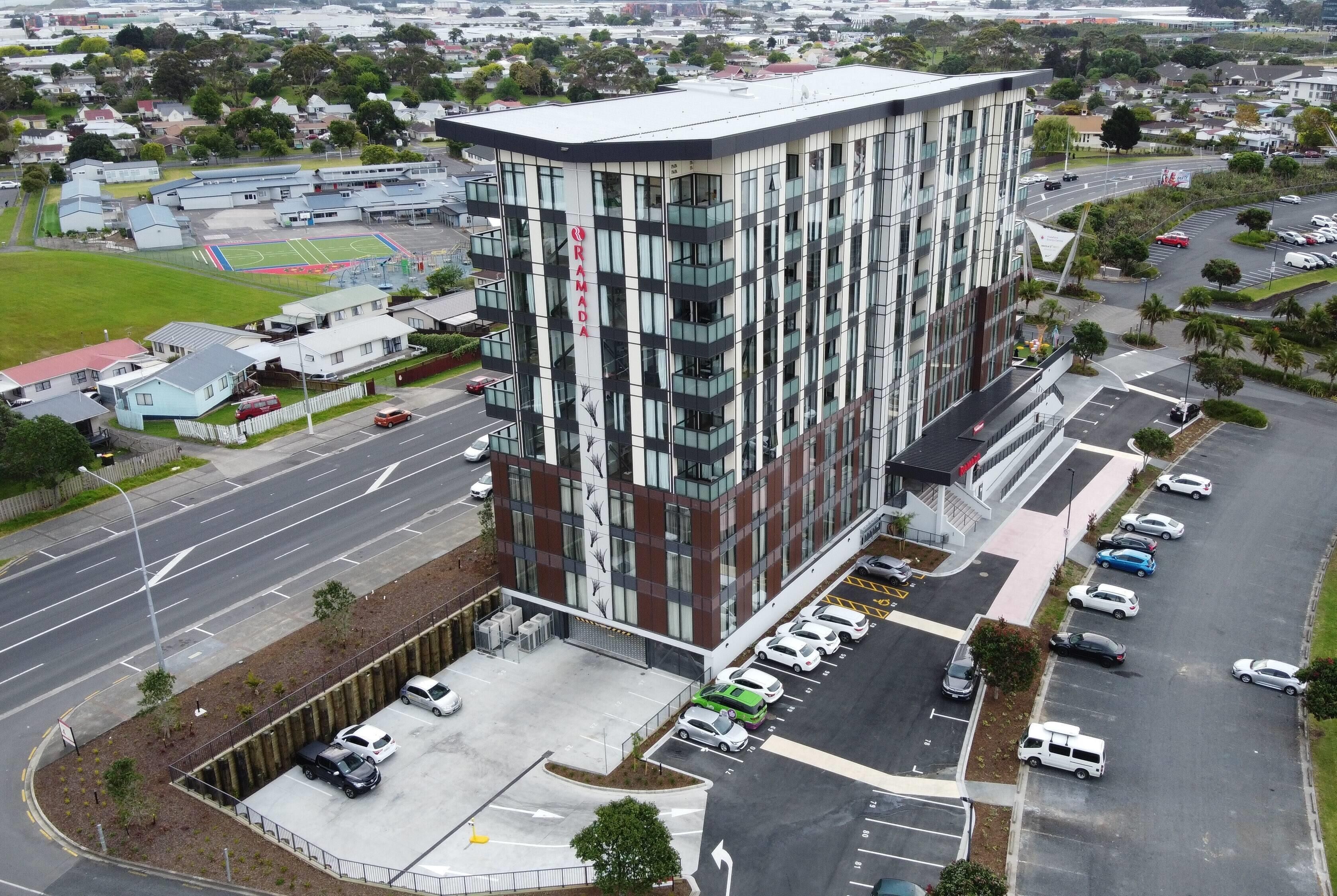 Un bâtiment moderne, reconnaissable à son grand panneau « Ramada », entouré d’un parking et bordé par une route.