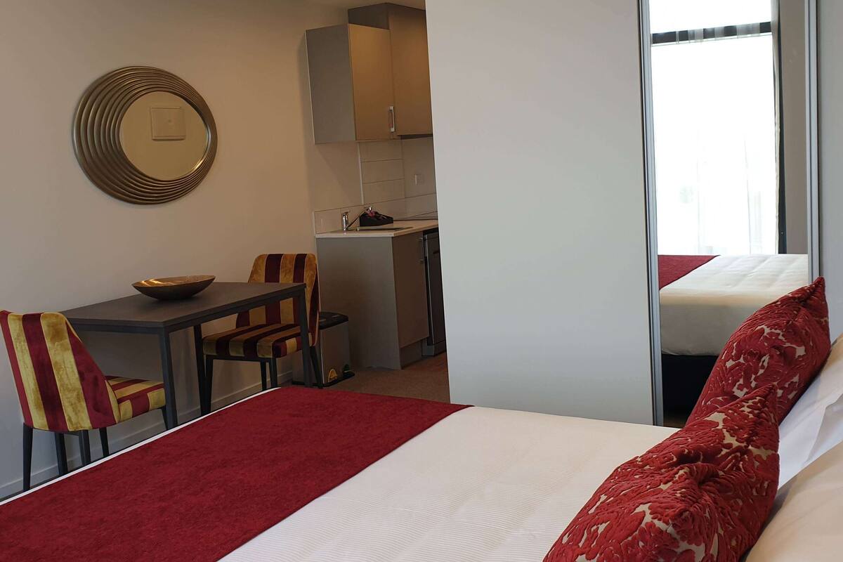 Ein Hotelzimmer mit einem Bett, einem Essbereich mit Tisch und Stühlen, einer Küchenzeile und einem Fenster.