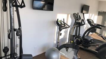 Une salle de sport à domicile équipée de matériel d’exercice, d’un téléviseur et d’un grand ballon de gymnastique.