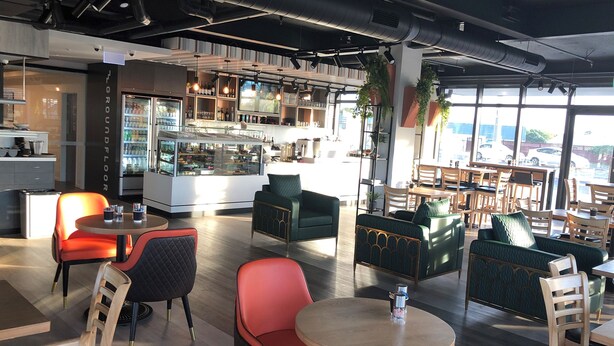 Un café moderno con mesas, una barra y amplios ventanales que dejan entrar luz natural.