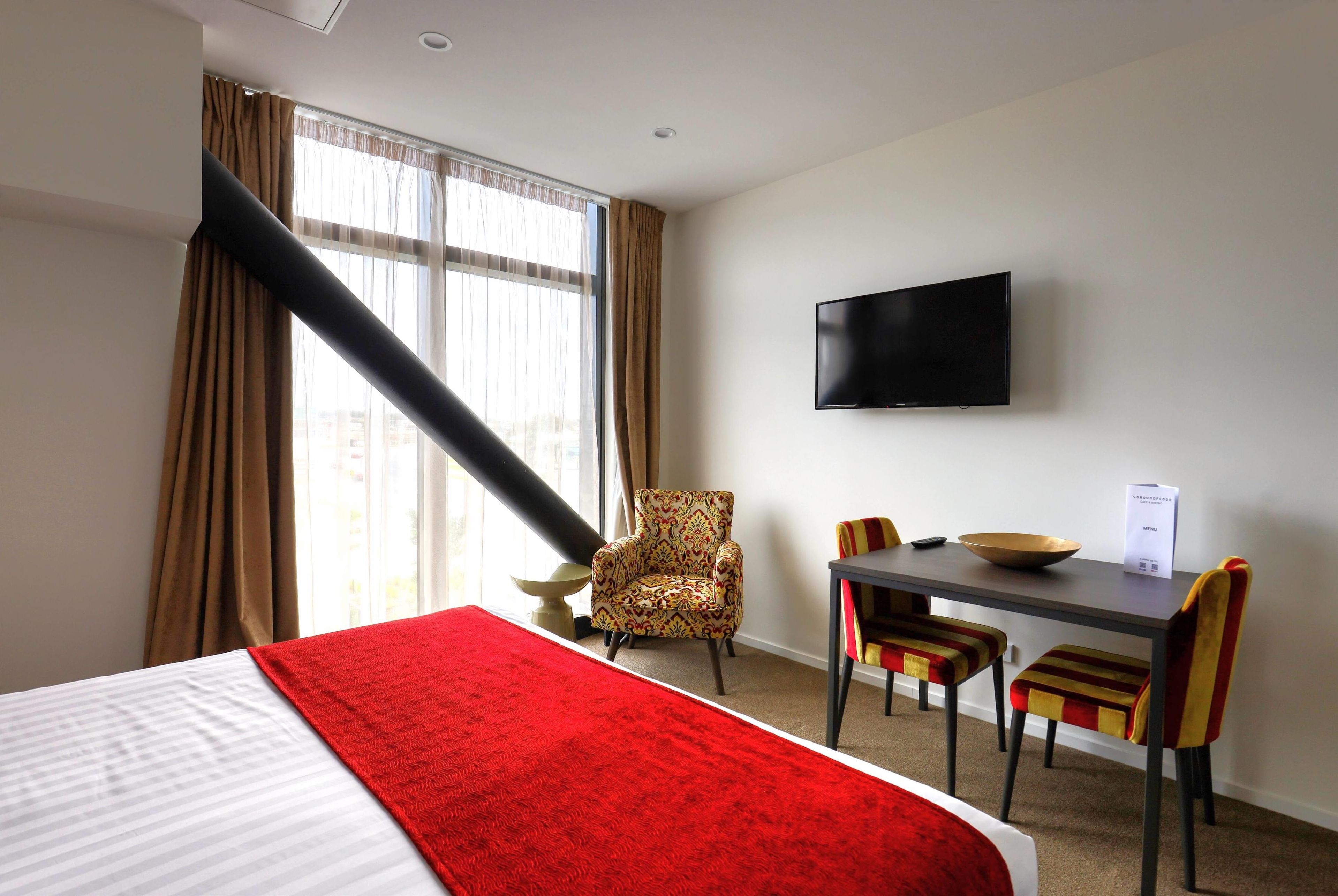 Habitación de hotel con cama, escritorio con sillas, televisor y ventana con cortinas.