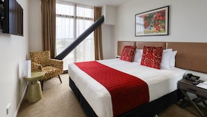 Habitación de hotel con una cama grande, una silla, una mesita, un televisor y un cuadro en la pared.