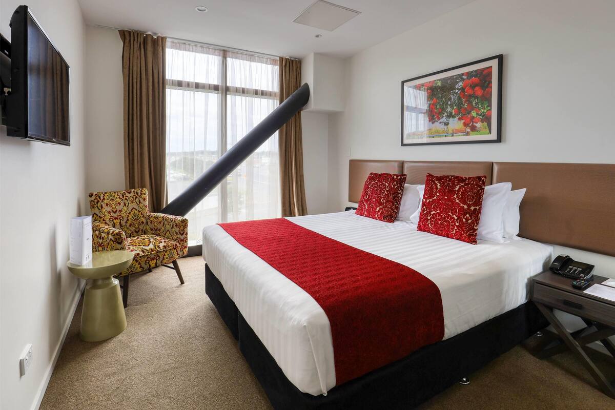 Ein Hotelzimmer mit einem großen Bett, einem Sessel, einem kleinen Tisch, einem Fernseher und einem Bild an der Wand.