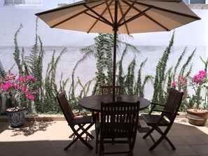 Relax in the serene patio area with a round table and four chairs, surrounded by lush greenery and a flowering plant.