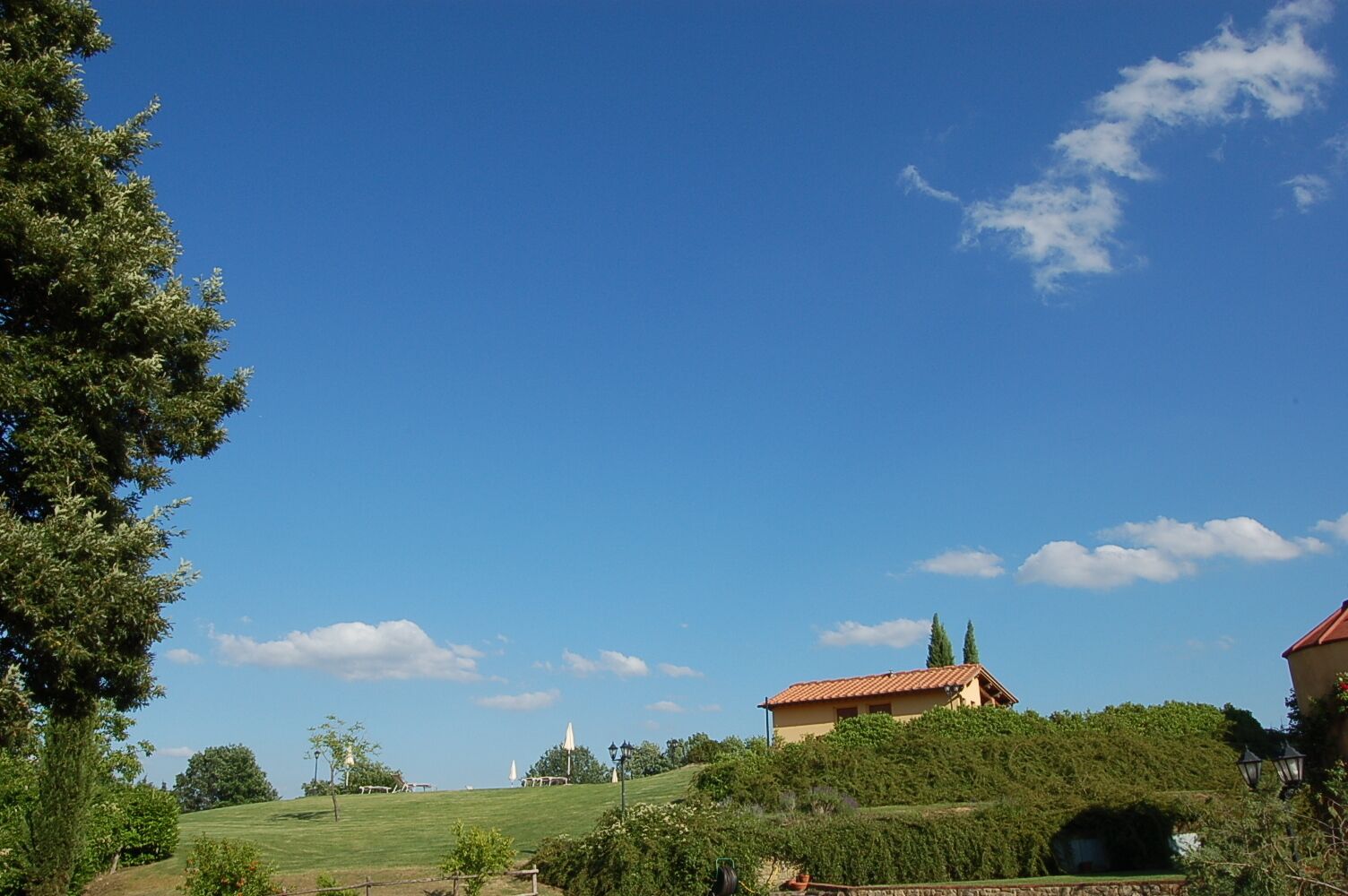 A rural landscape with a house on a hill, a clear blue sky, and a small church in the distance.