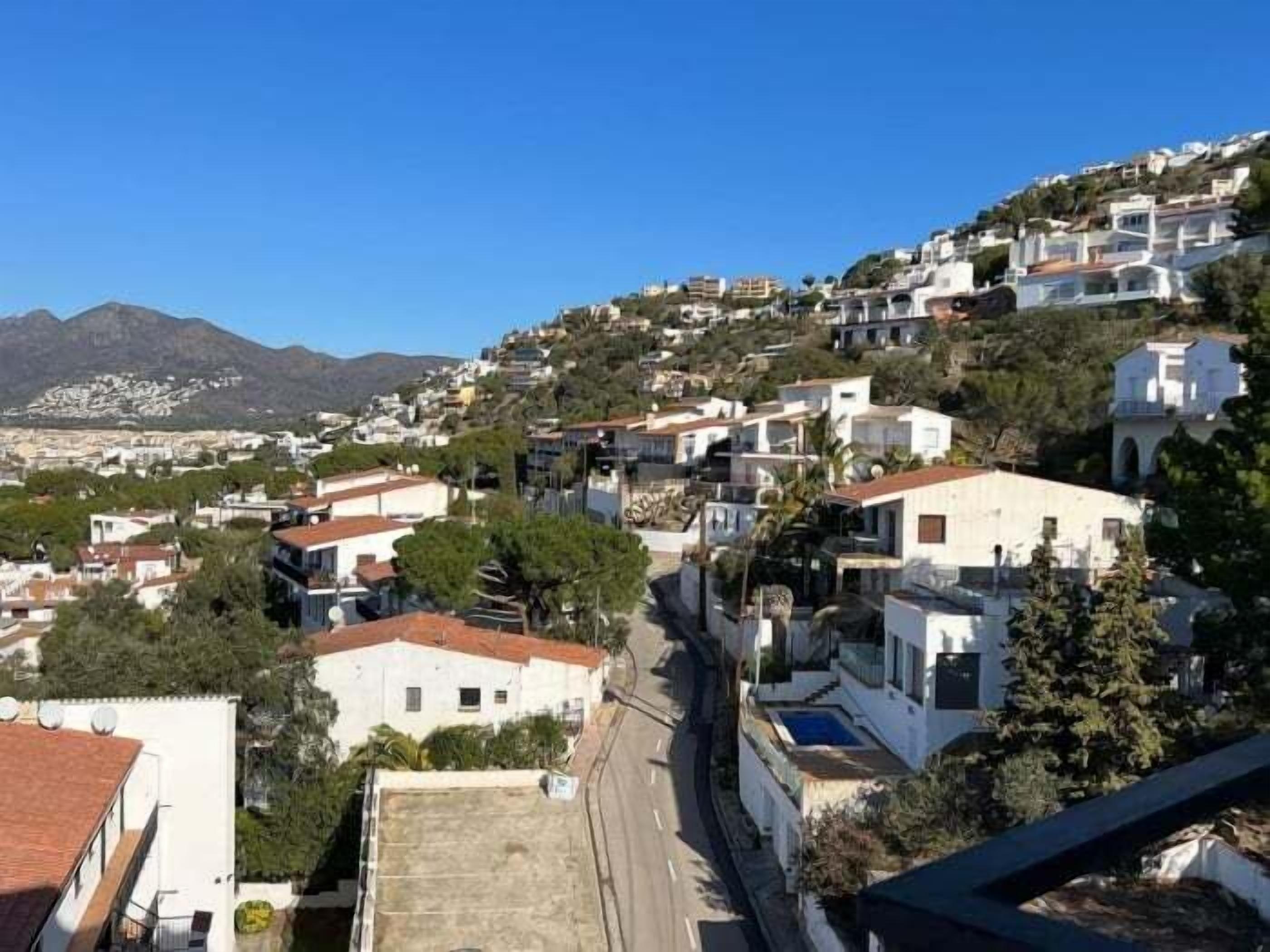 Un quartier résidentiel situé sur une colline, avec des bâtiments blancs, une route dégagée et une montagne en arrière-plan.