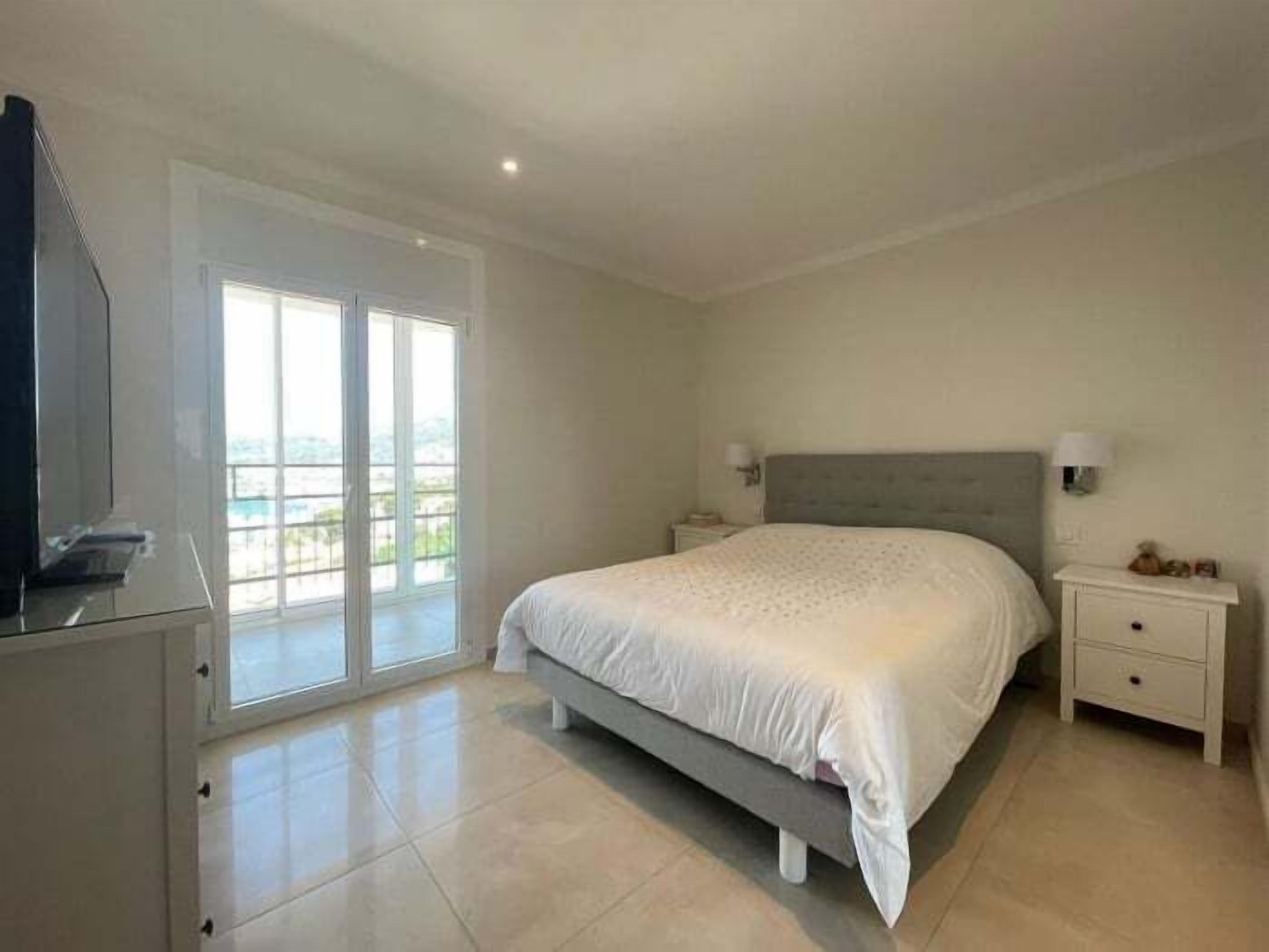 A bedroom with a large bed, a TV, a sliding glass door, and a nightstand with a lamp.