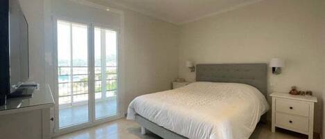 A bedroom with a large bed, a TV, a sliding glass door, and a nightstand with a lamp.