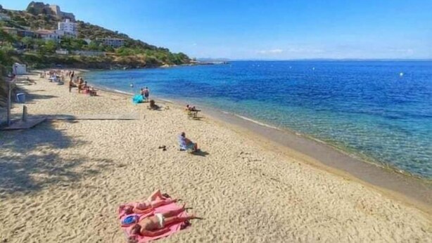 A beach with clear blue water, a sandy shore, and a building on a hill in the background. - Lovely flat with views Roses Av 48 (Rosas / Roses)