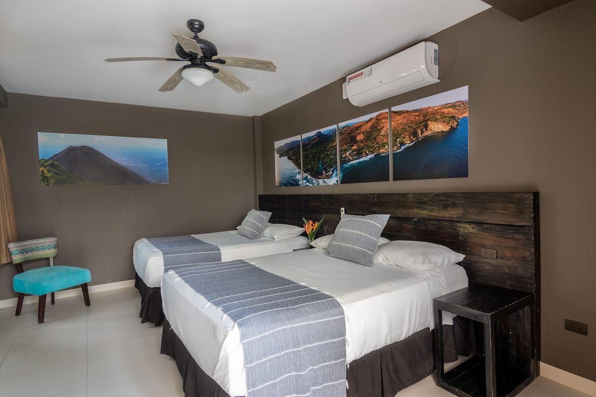 A bedroom with two beds, a ceiling fan, an air conditioner, and wall art depicting landscapes.