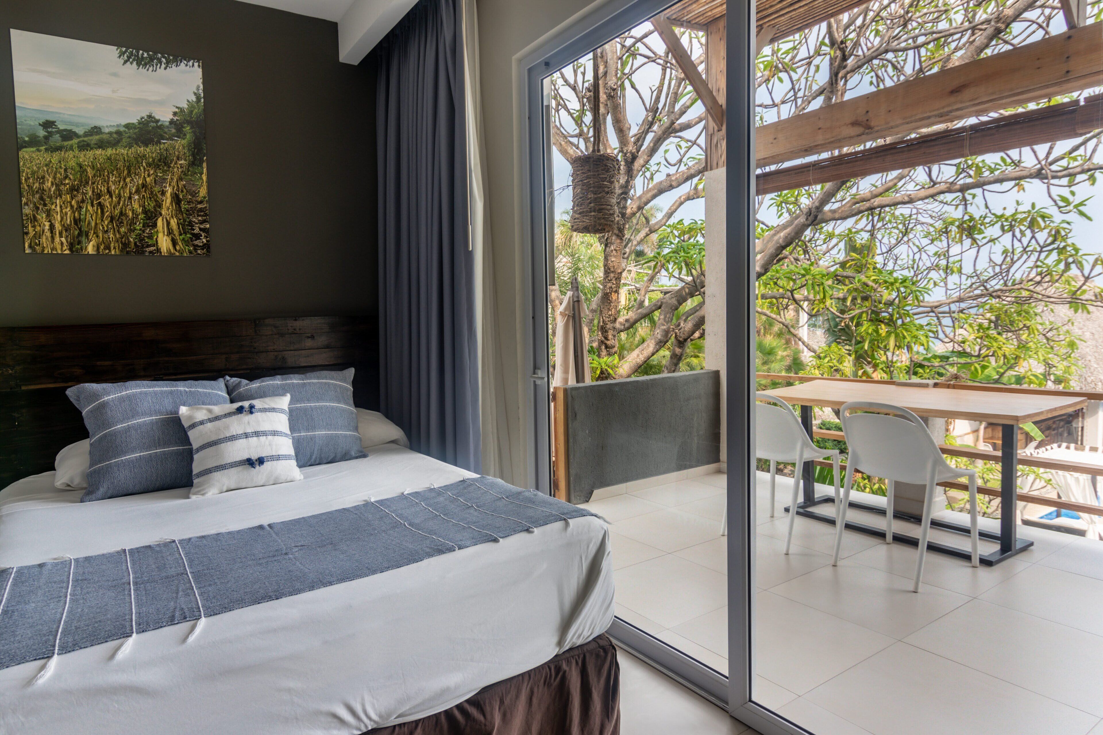 A bedroom with a bed, a view of the outdoors through a sliding glass door, a table, and chairs.