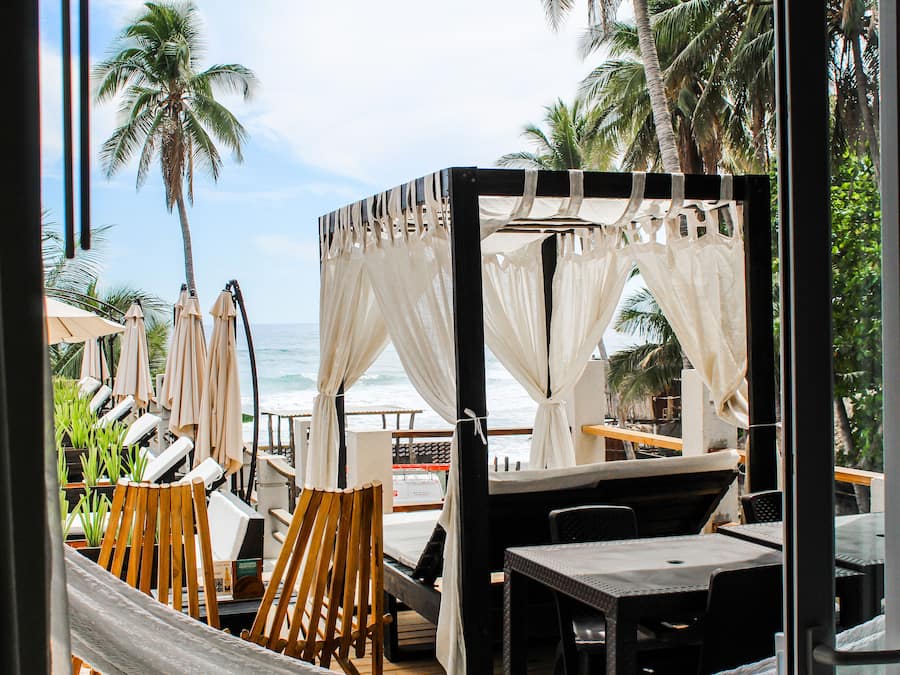 Een restaurant aan het strand met terras, inclusief houten stoelen en tafels, en uitzicht op de oceaan.