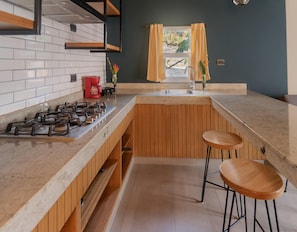 A kitchen with a wooden countertop, a gas stove, a sink, and two bar stools.