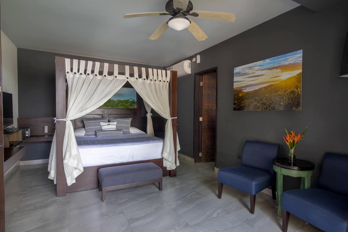 A bedroom with a four-poster bed, a ceiling fan, a nightstand, a bedside table, a chair, and a small table with a vase of flowers.