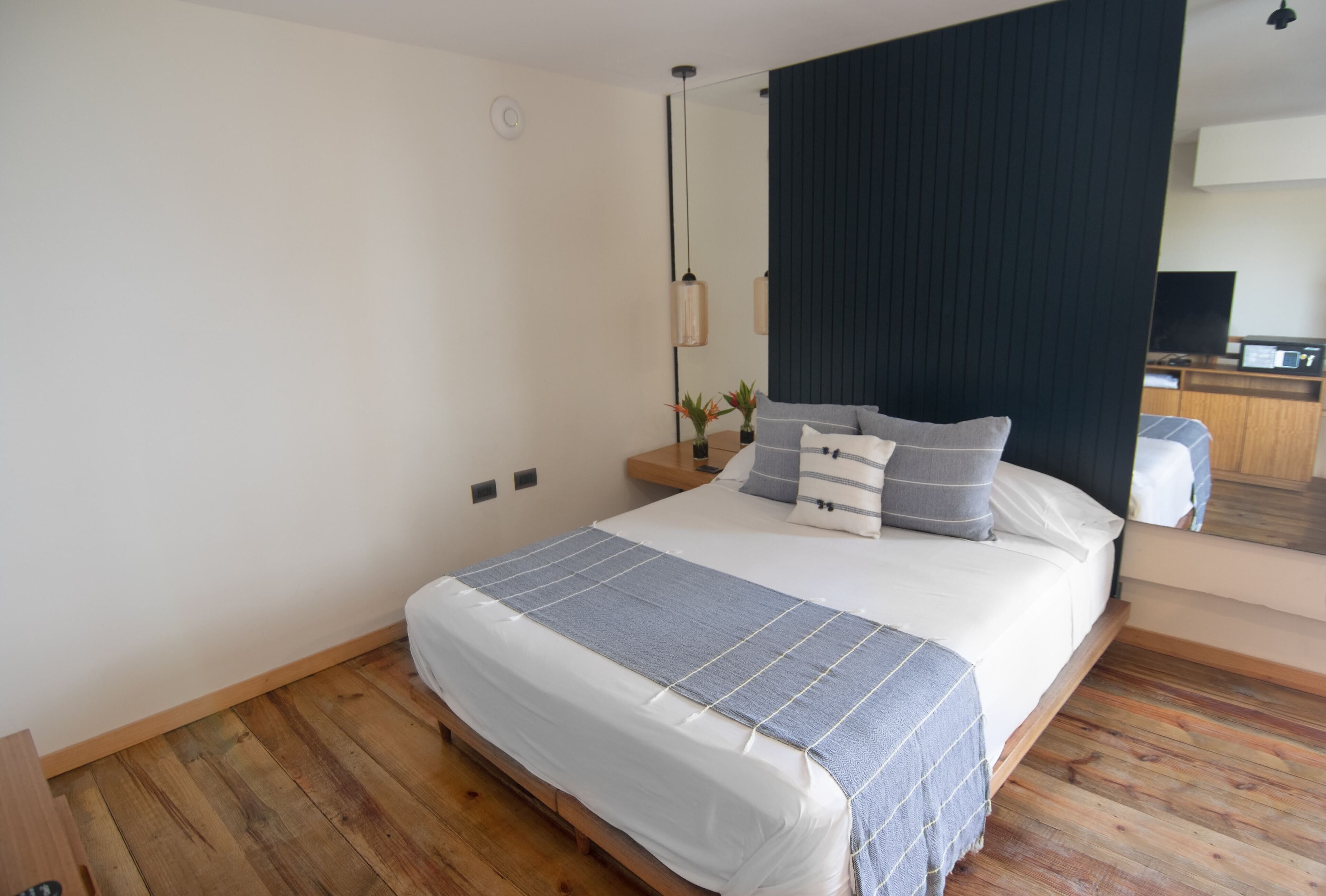Une chambre à coucher moderne avec un grand lit, un plancher en bois, un mur d’accent de couleur foncée et une table de chevet avec une lampe.