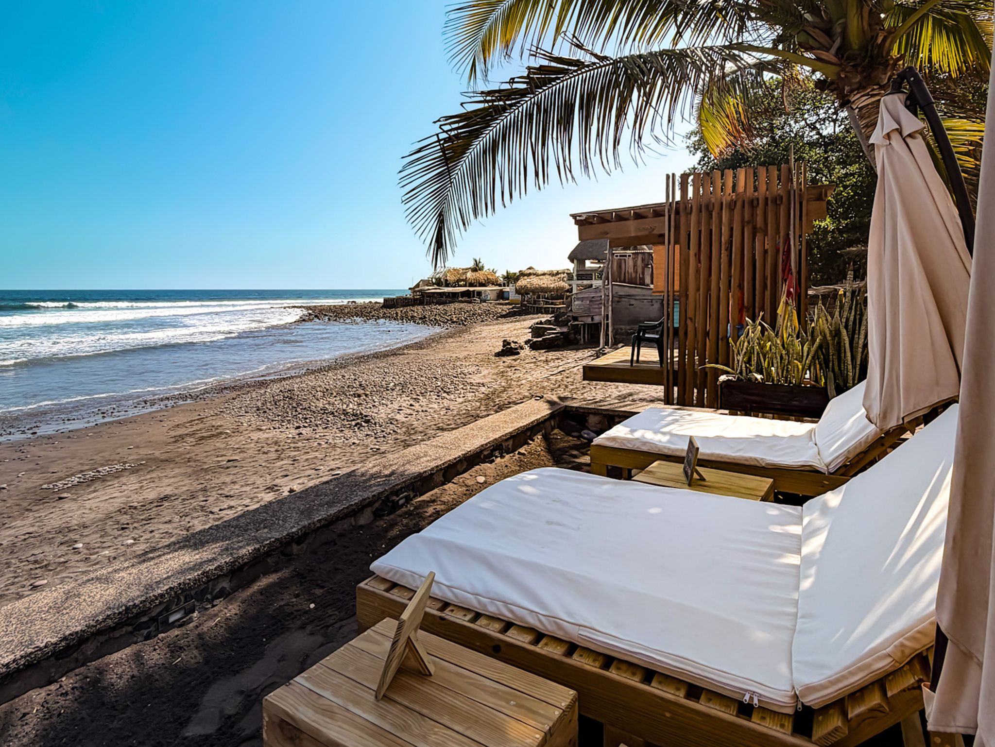 A beachside accommodation with wooden beds, a thatched-roof structure, and a view of the ocean.